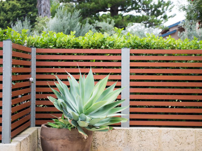 Timber louvre fencing in Perth. A wood-look timber fence with a plant pot in front of it.