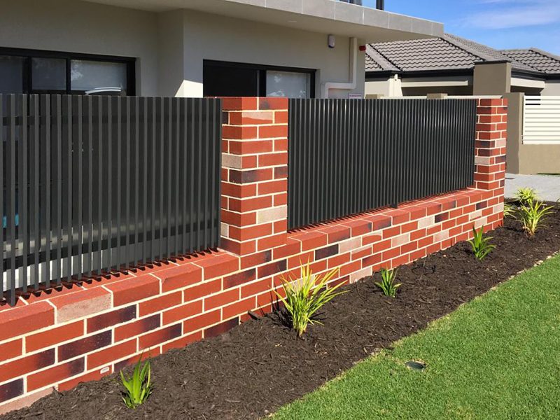 A red brick retaining wall with black blade fencing outside a Perth home